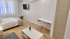 Una habitación moderna y luminosa con una cama, un sofá, una pequeña mesa de centro, un escritorio y un televisor fijado a la pared.