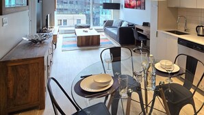 A modern kitchen with a dining area, a sofa, and a view of the city.