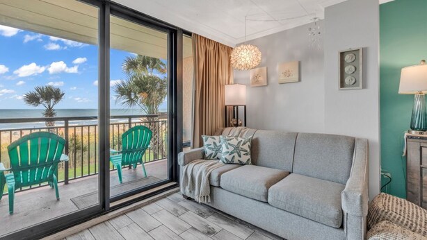A balcony with a view of the ocean, a grey sofa, green chairs, and a ceiling light fixture. - The Caravelle Resort (Myrtle Beach)