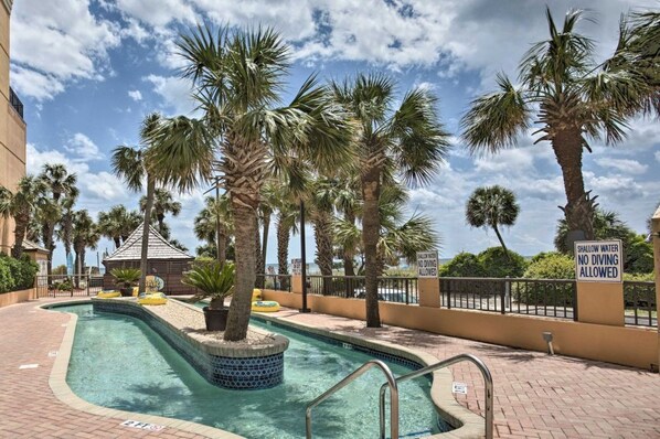 A swimming pool surrounded by palm trees, with a sign indicating shallow water and no diving allowed.