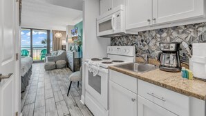 A modern kitchen with white cabinets, a granite countertop, a built-in microwave, and a coffee maker. - The Caravelle Resort (Myrtle Beach)
