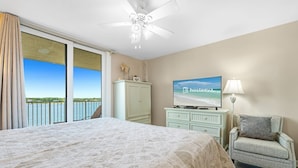 A bedroom with a large bed, a television, a chair, and a view of the sea.