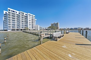 A wooden pier extending into calm water, leading to a white multi-story building with balconies. - Compass  Point  508 (Gulf Shores)