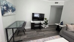 Ein modernes Wohnzimmer mit Glastisch, schwarzem Sofa, Flachbildfernseher und großem abstrakten Gemälde an der Wand.