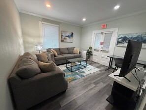 A living room with a sofa, a coffee table, a TV, and a door with an emergency exit sign.