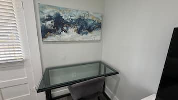 Ein Zimmer mit Glastisch, einem Stuhl, einem Gemälde an der Wand und einem Fernseher auf einem Schrank.