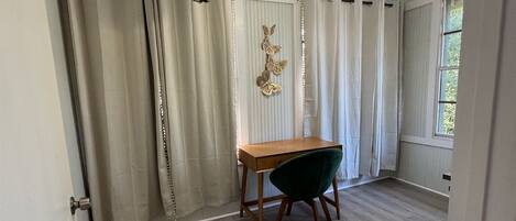 Una stanza con una scrivania in legno, una sedia verde, un ventilatore a soffitto e una finestra con tende.