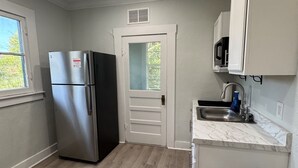 A compact kitchen with a stainless steel refrigerator, a built-in microwave, and a sink with a marble countertop.