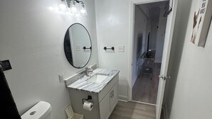 A modern bathroom with a toilet, sink, and mirror. There is a shower area visible in the background.