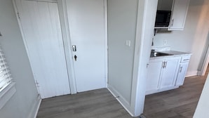 A hallway with a wooden floor, white doors, and an exit sign. A welcome mat is visible at the entrance.
