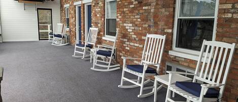 A covered patio with white rocking chairs and a model ship.