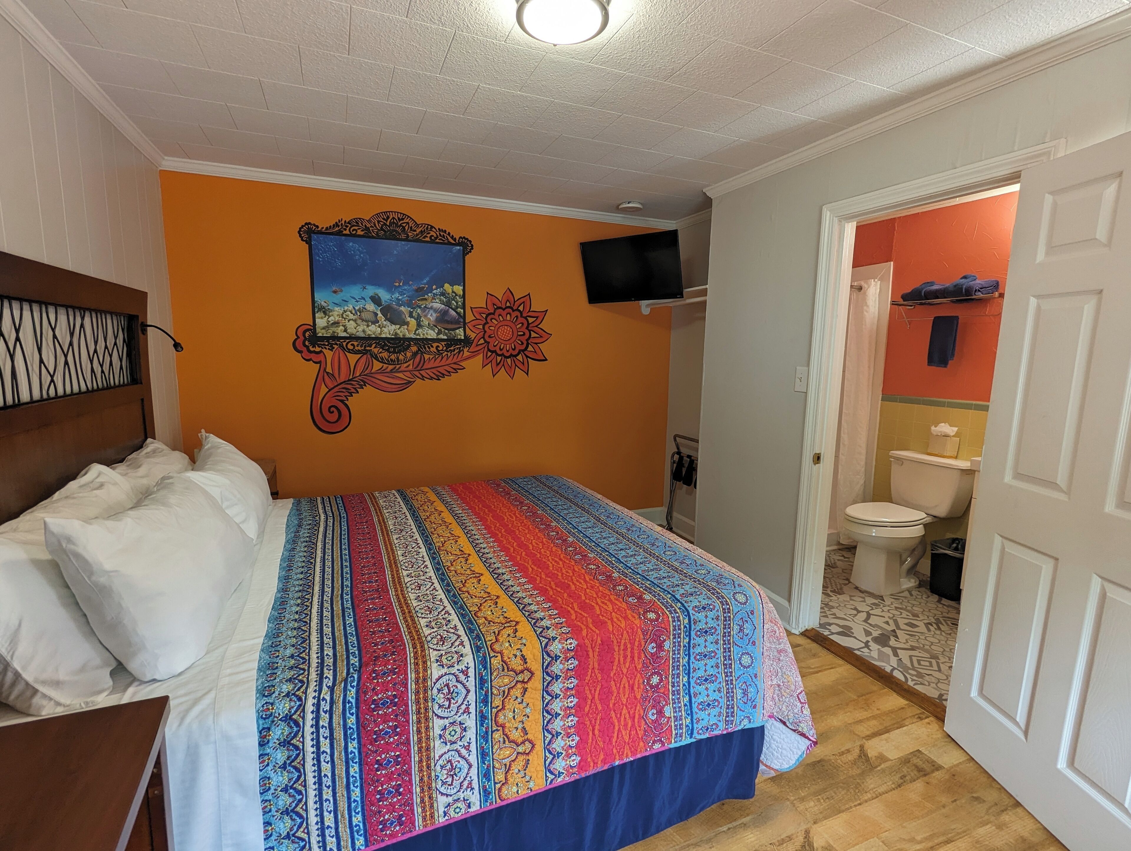 A hotel room with a bed, a television mounted on the wall, and a bathroom visible through an open door.