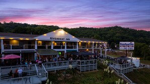 A Riverboat Inn with a covered deck area, outdoor seating, and a signboard advertising amenities like a bar, pool, and WiFi.