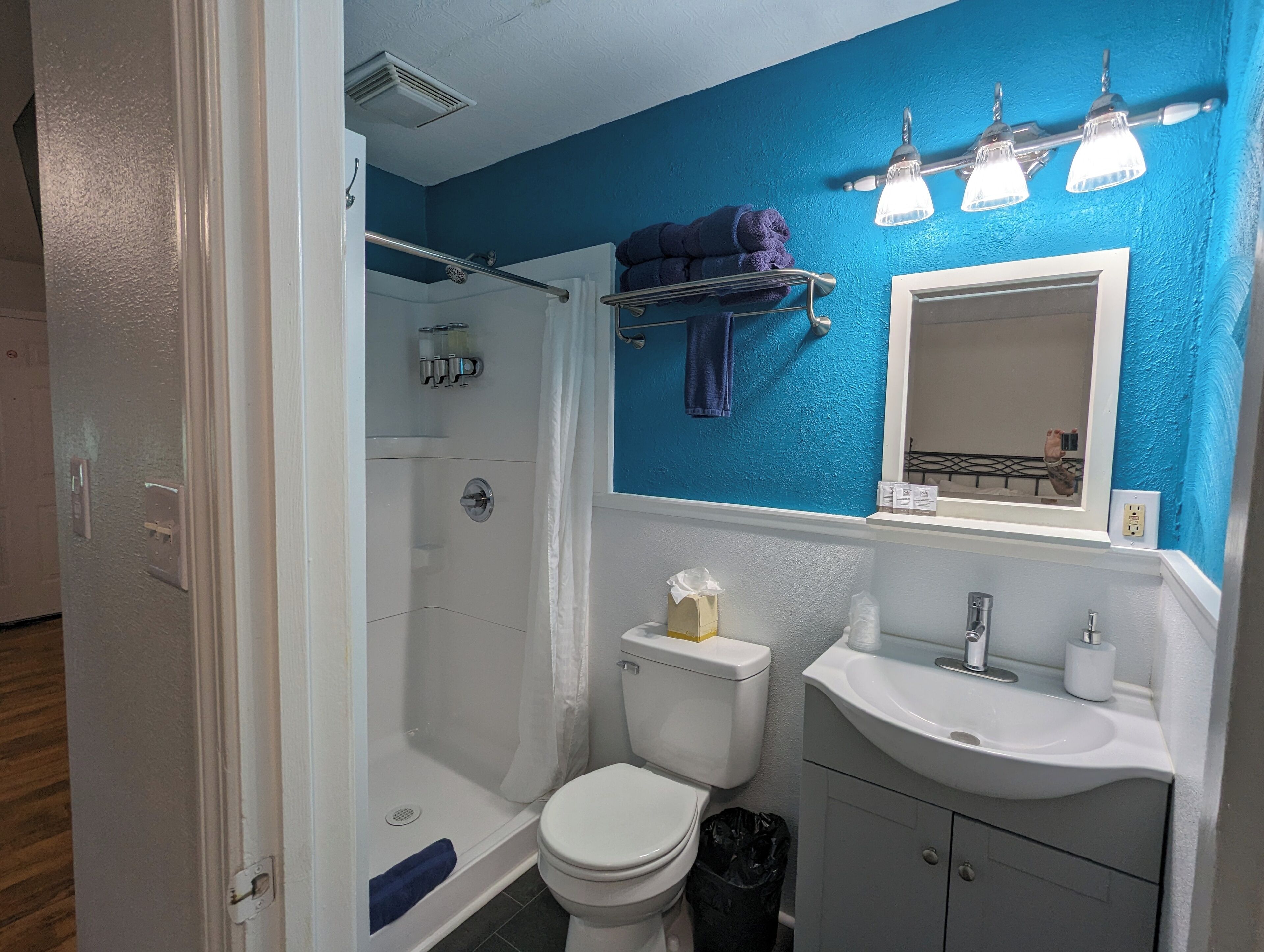 Un baño con ducha, inodoro, lavamanos y una pared azul decorativa.