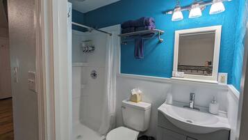 Un baño con ducha, inodoro, lavamanos y una pared azul decorativa.