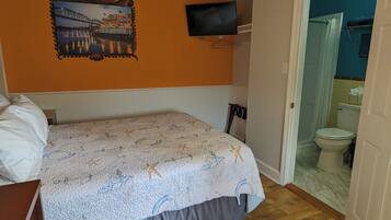 A room with a bed, a mounted TV, and a wooden ceiling.