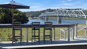 A deck with two chairs and a table, overlooking a river and a bridge.