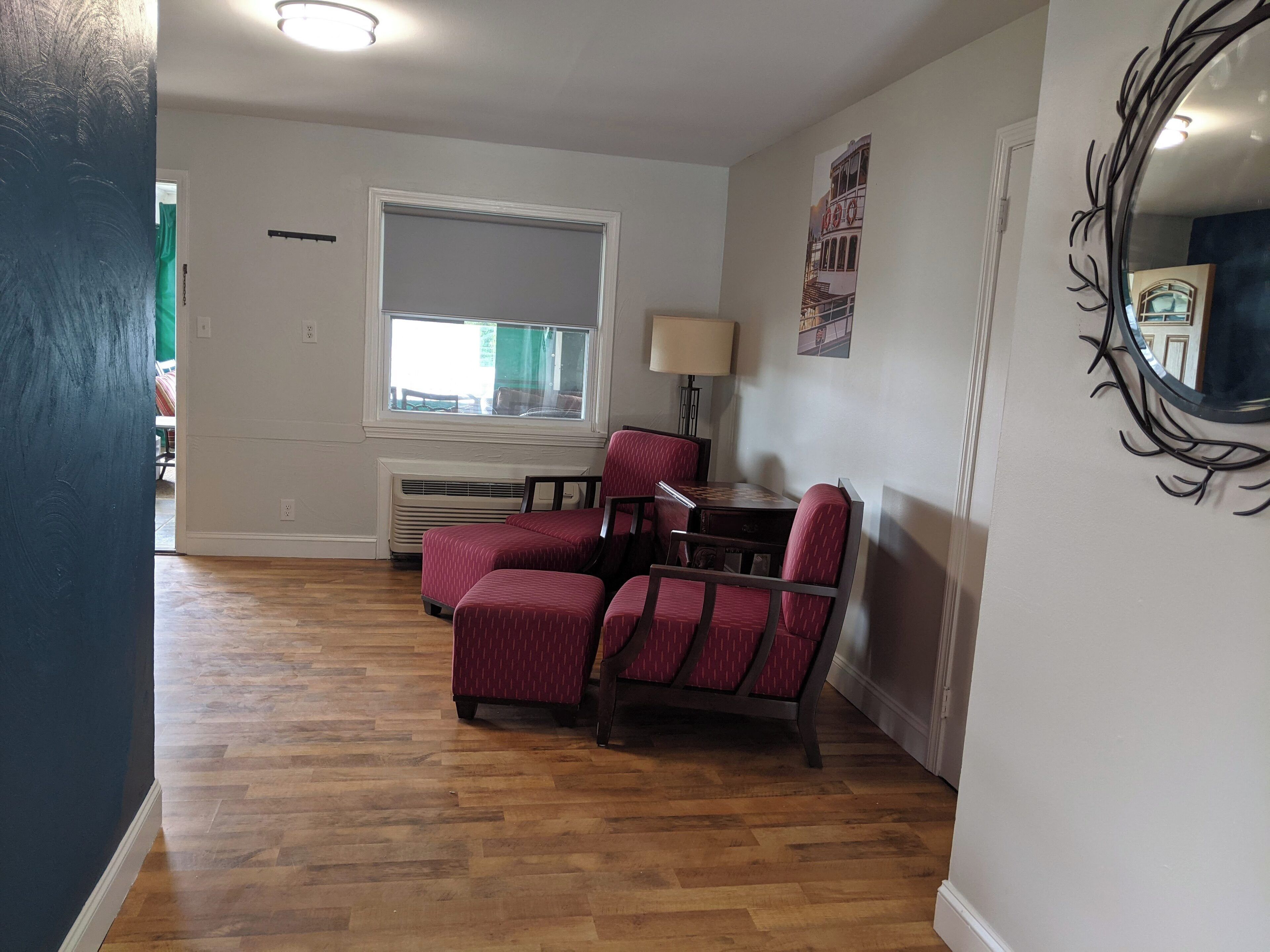 A living room with a large window, a fireplace, and a dining area with two red upholstered chairs.