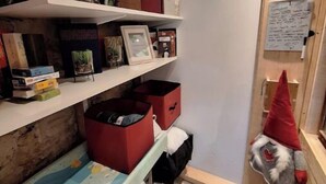 A narrow hallway with wooden flooring, shelves filled with books and storage boxes, and a gnome decoration on the wall. - Atypical little gîte chez sam est gael  (Charix)
