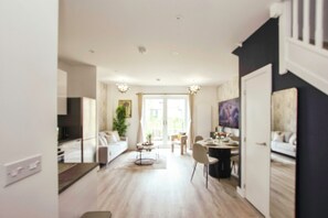 A modern living room with a sofa, dining table, and chairs. There is a staircase leading to another level. - Apricot House- Cozy 2 Bedroom House in Birmingham (Birmingham)