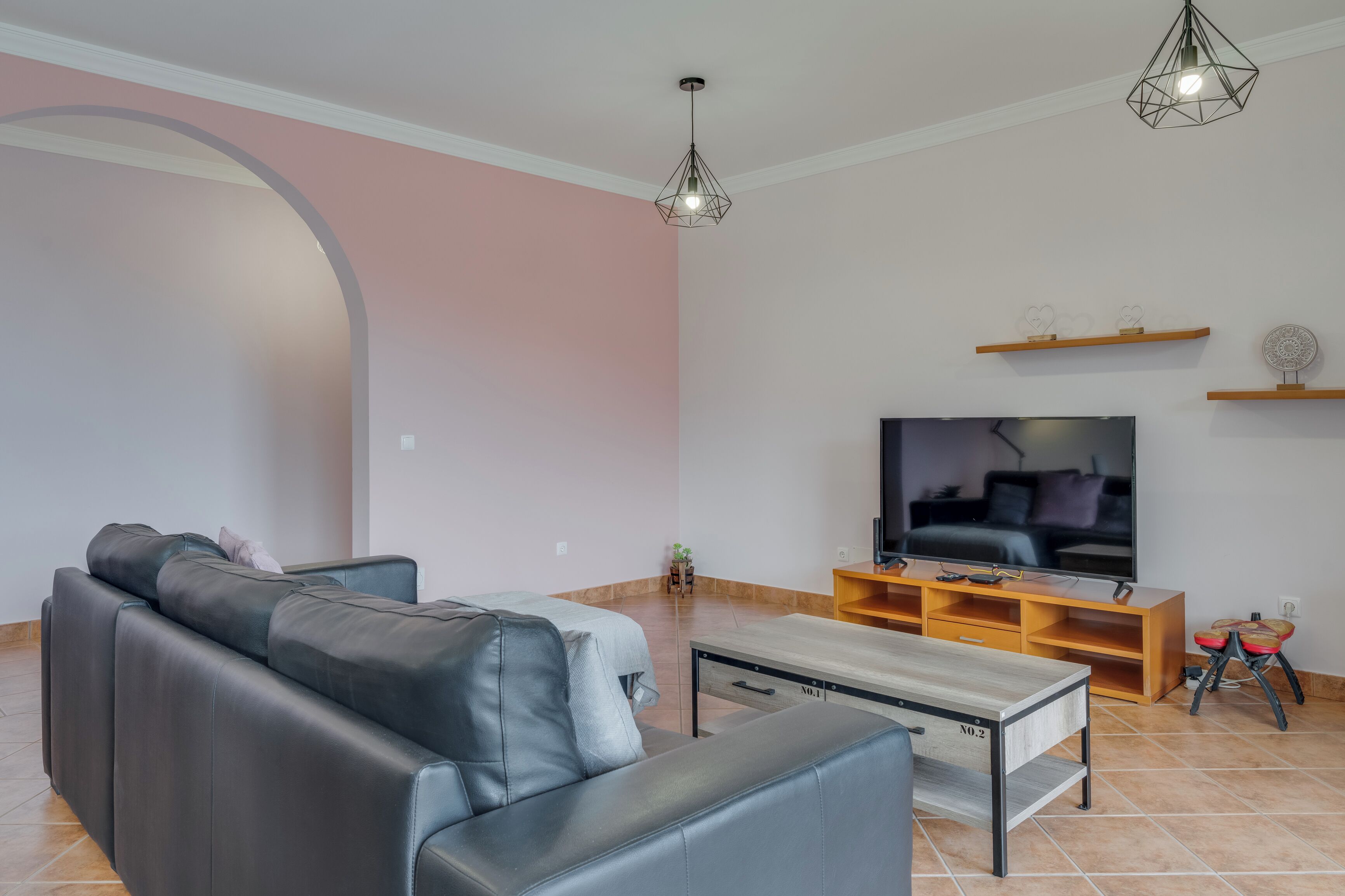 A modern living room with a sofa, TV, wooden entertainment unit, and a unique ceiling light fixture.