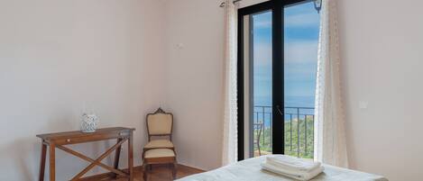 A bedroom with a bed, a chair, a small table, and a window with curtains.