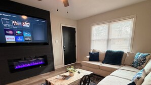 A modern living room with a flat-screen TV, a ceiling fan, a fireplace, a sofa, and a coffee table. - Quiet & Private, Comfy Beds, Fire Pit, & Bikes

 (Portsmouth)
