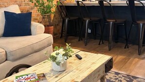 A living room with a sofa, a coffee table, and a kitchen area with a counter and chairs. - Quiet & Private, Comfy Beds, Fire Pit, & Bikes

 (Portsmouth)