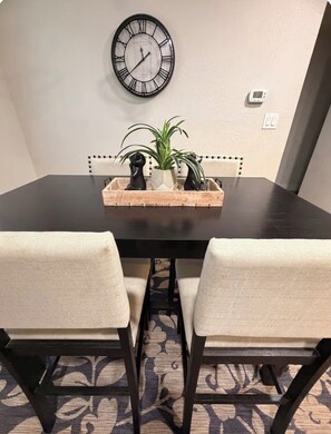 A dining table with two chairs, a wall clock, and a plant centerpiece.