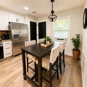 A modern kitchen with a dark wooden table, white chairs, and a stainless steel refrigerator.