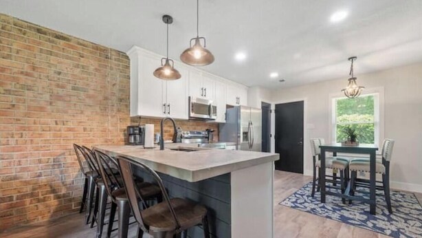 A kitchen with a brick accent wall, pendant lighting, and a dining area with a table and chairs. - Quiet & Private, Comfy Beds, Fire Pit, & Bikes

 (Portsmouth)