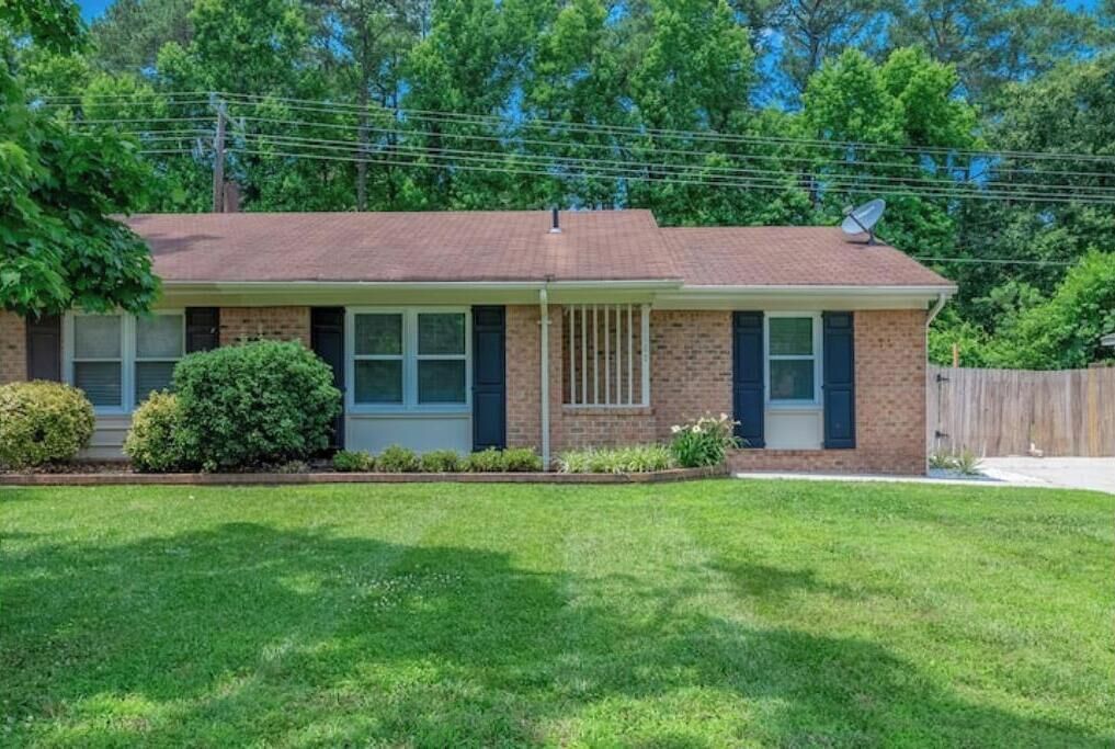 A single-story brick house with a front porch, a satellite dish, and a well-maintained lawn.