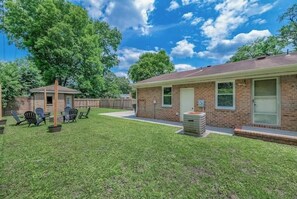 A single-story brick building with a small attached garage, a covered patio with chairs, and a well-maintained lawn.