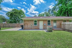 A single-story brick building with a front door, a small porch, and a trash can in the yard.