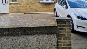 A two-story residential building with a brick facade, a white car parked in the driveway, and a clear blue sky in the background. - 5 Bed Family Home Greater London, Free Parking (Romford)
