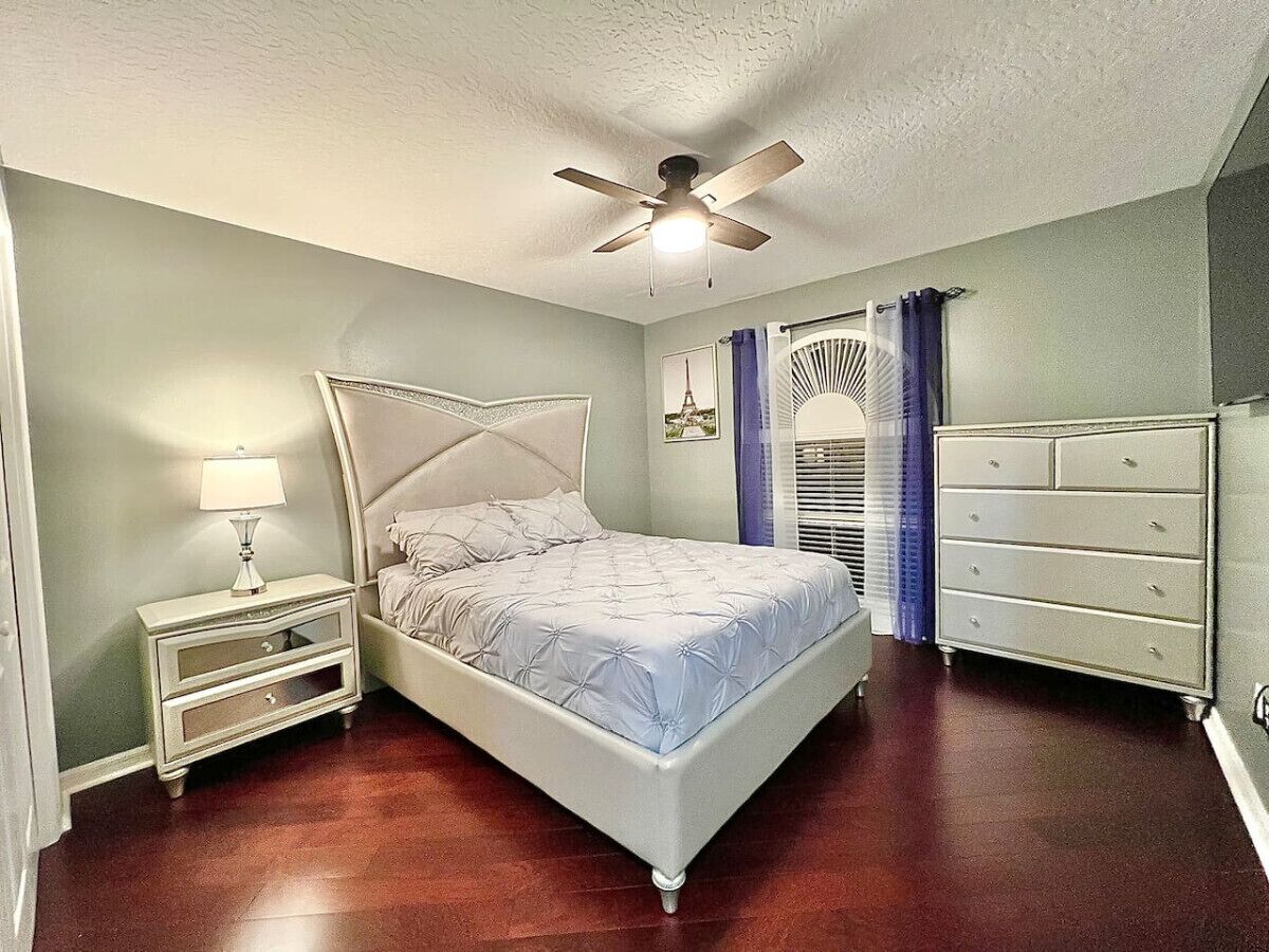 Un dormitorio con cama, mesita de noche, cómoda y ventilador de techo.