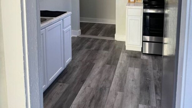Una cocina con armarios blancos, horno de acero inoxidable y piso de madera.