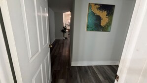 Un pasillo con piso de madera, una puerta blanca y un cuadro colgado en la pared.