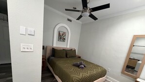 Un dormitorio con cama, ventilador de techo, mesita de noche, espejo y puerta.