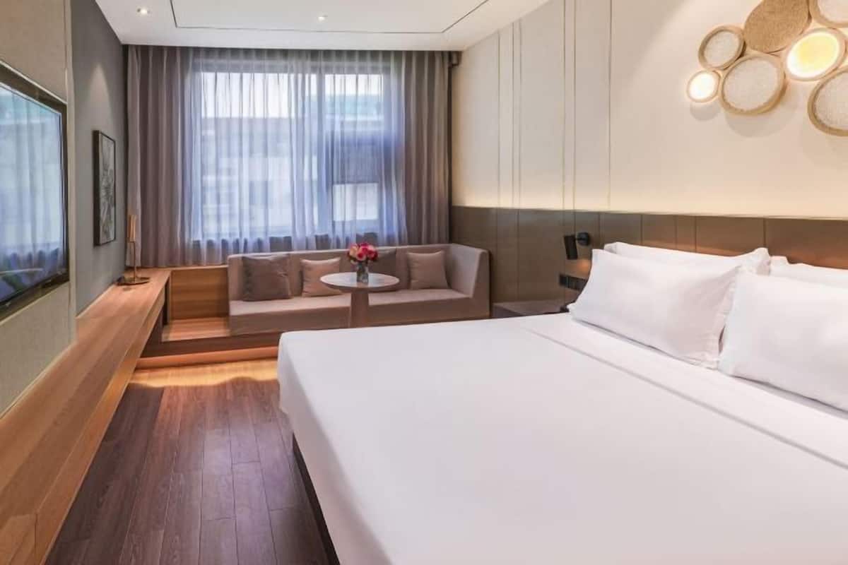 A hotel room with a large bed, a sofa, a small table with flowers, and a TV on the left wall.