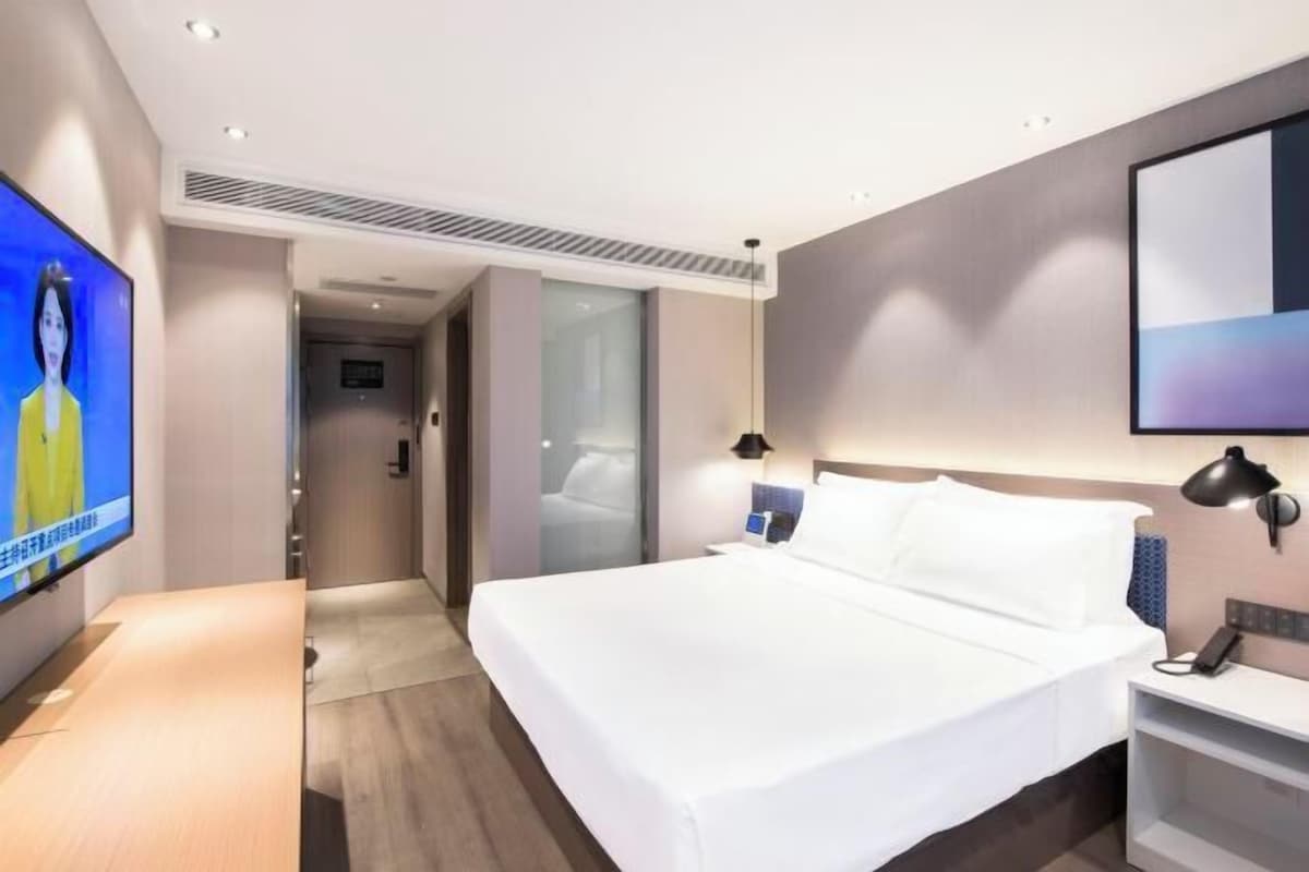 A modern hotel room with a large bed, a flat-screen TV, a desk, and a bedside table.