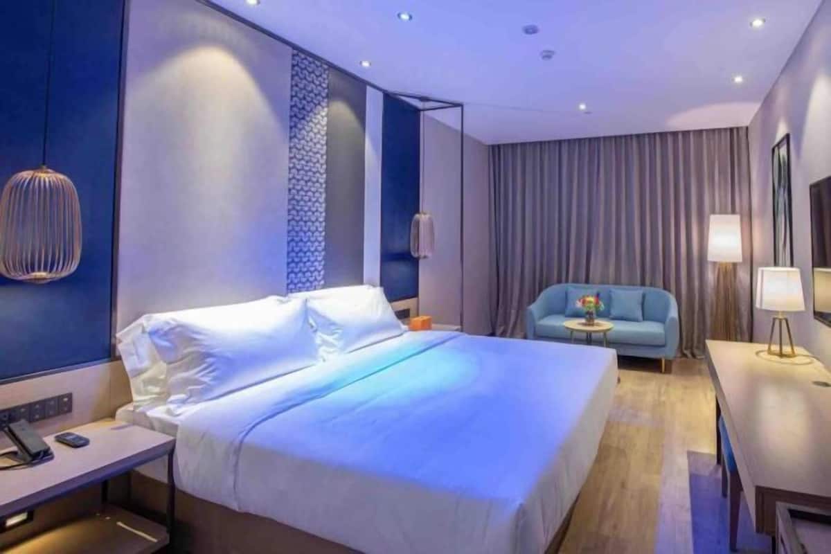 A hotel room with a bed, a desk, a chair, a sofa, and a TV.