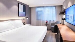 A hotel room with a large bed, a desk, a chair, a small table with a vase of flowers, a TV, and a window with curtains. - Orange Hotel (Zhengzhou Hongzhuan Road) (Zhengzhou)