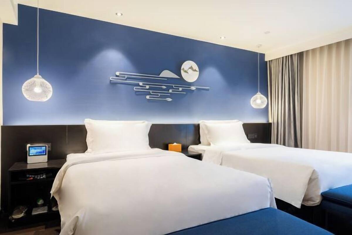 A hotel room with two beds, a wall-mounted artwork, a nightstand with a clock, and a curtain.
