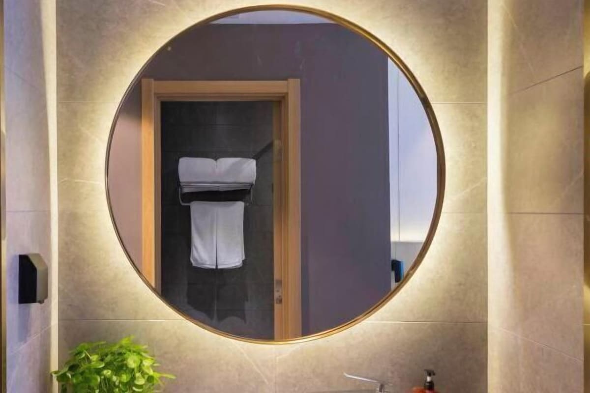 A circular mirror with a wooden frame, a towel hanging inside, and a plant below it.