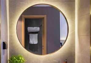 A circular mirror with a wooden frame, a towel hanging inside, and a plant below it. - Orange Hotel (Zhengzhou Hongzhuan Road) (Zhengzhou)