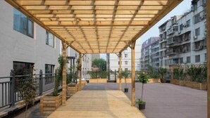A covered outdoor area with wooden flooring, potted plants, and a view of residential buildings in the background. - Orange Hotel (Zhengzhou Hongzhuan Road) (Zhengzhou)