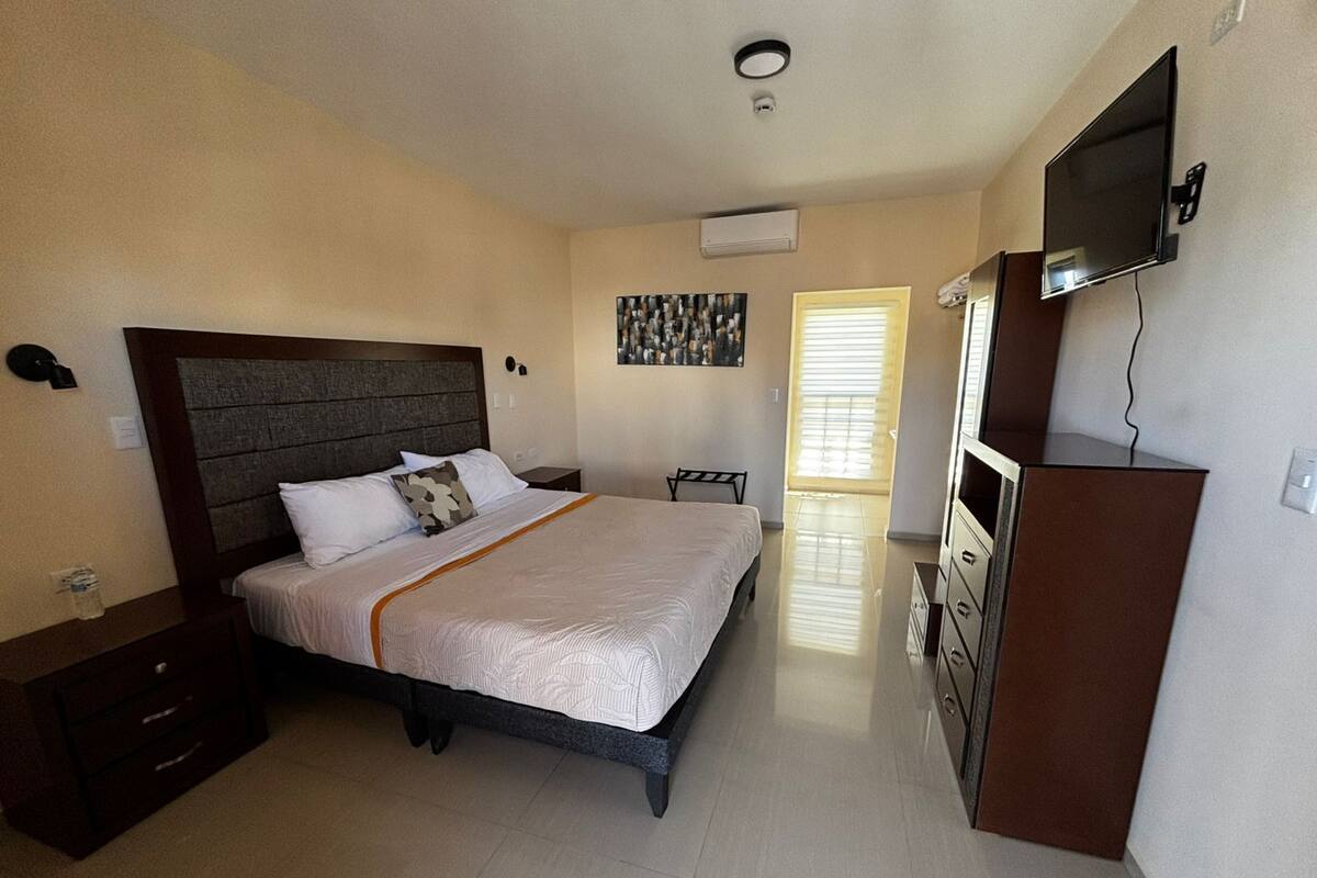 A hotel room with a bed, a TV, a dresser, and a painting on the wall.