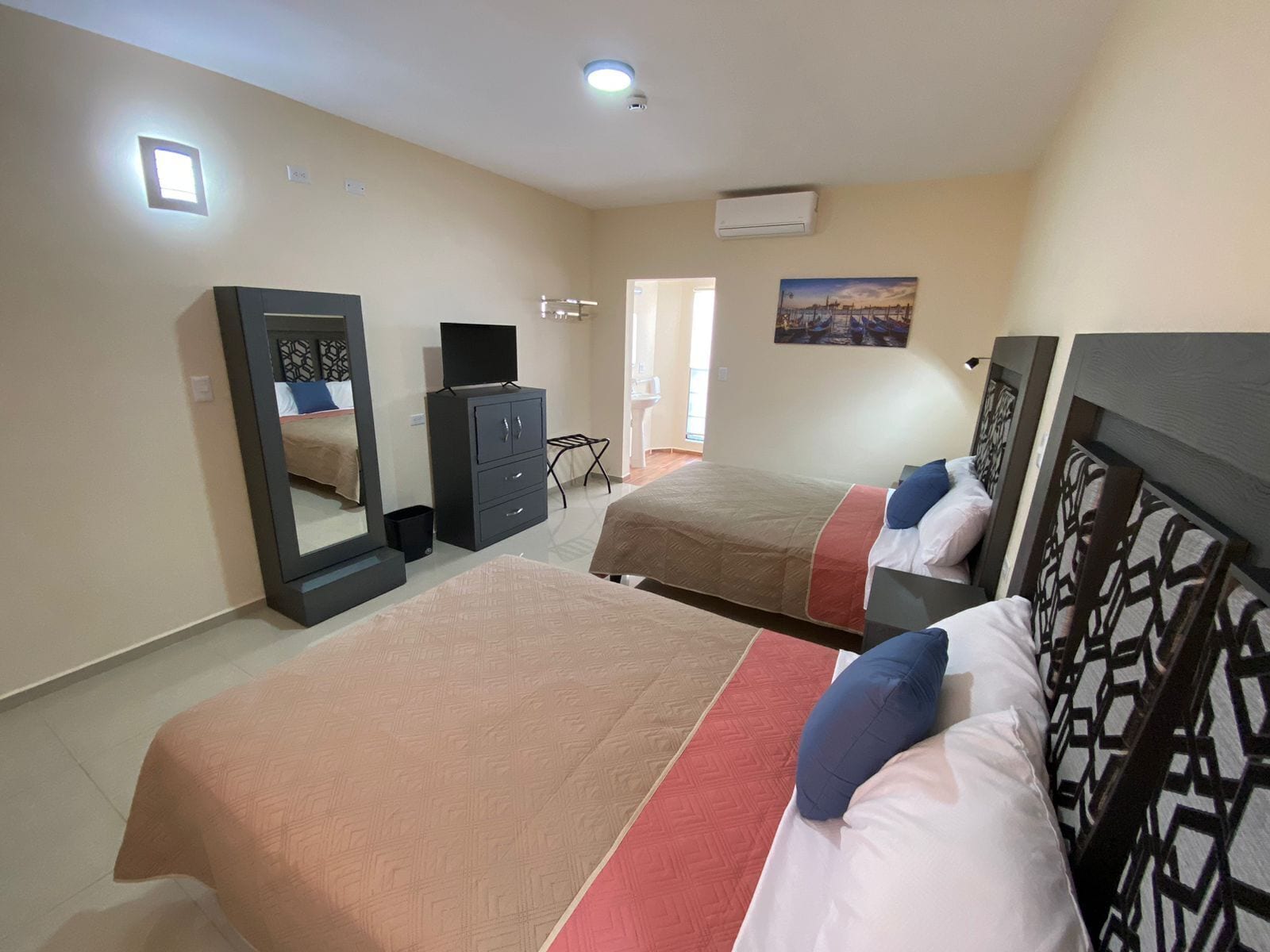 A bedroom with two beds, a wardrobe, a mirror, and an air conditioning unit.