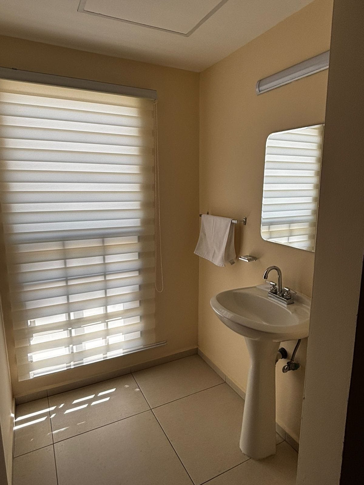 A bathroom with a sink, mirror, and window with blinds.